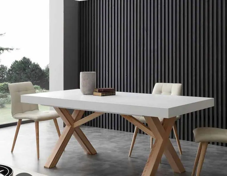 Mesa de jantar branca com pés cruzados em madeira diante de painel ripado preto